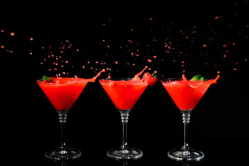 Glasses of delicious strawberry daiquiri with splash on black background