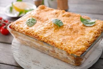 Tasty lasagna in baking dish on wooden board