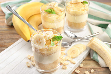 Glasses with delicious banana pudding on wooden board