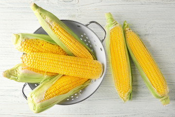 Colander and fresh corn cobs on wooden table