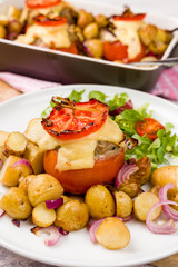 Oven baked tomatoes stuffed with minced meat, cheese and herbs. Served with new potatoes and salad. Casserole oven dish visible on white wooden background