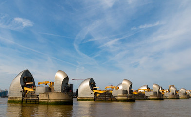 The metallic Thames Barrier gates and piers on a summers day with wispy clouds in the sky in Greenwich London.
