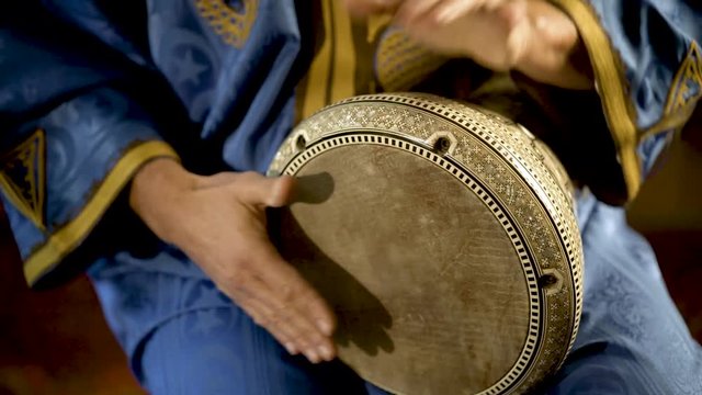 Tight shot of man in Moroccan dress playing arabic doumbek, darbuka, or derbeki