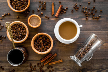 Cup of milky coffee near coffee beans and cinnamon on wooden background top view