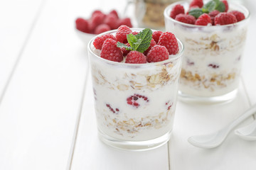 Healthy dessert with yogurt, muesli and raspberry in glasses on white wooden table.