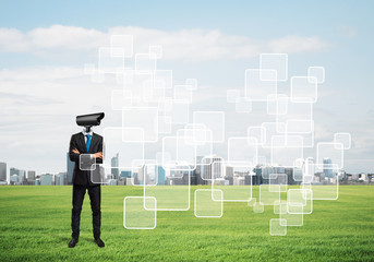 Camera headed man standing on green grass against modern cityscape