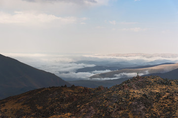 hiker the winner stands on the edge of a rock with sticks raised up in front of a valley covered by clouds in the Caucasus