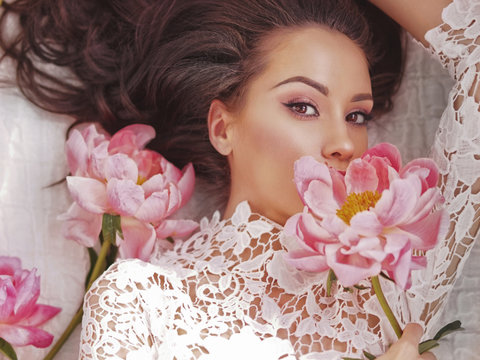 Beautiful young woman lies among peonies