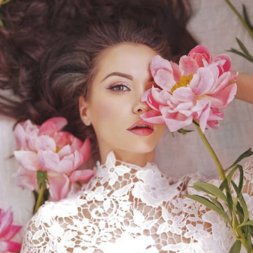 Beautiful young woman lies among peonies