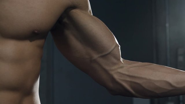 A fitness model tenses up his bicep muscle displaying its form. Close up.