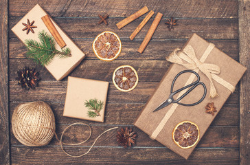 Set for Christmas gift wrapping. Presents wrapping inspirations. Gift box, ball of jute, cinnamon sticks, anise, orange slices, fer tree branches  and retro scissors on rustic wooden background. 