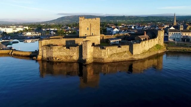 Medieval Norman Castle in Carrickfergus near Belfast in sunrise light. Aerial approach video with marina, town and far view of Belfast in the background