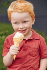 Portrait of cute white Caucasian redhead blond preschool boy with blue eyes in red t-shirt eating licking ice cream in waffle cone