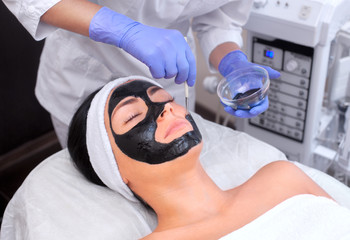 The procedure for applying a black mask to the face of a beautiful woman. Spa treatments and care of the cats in the beauty salon.