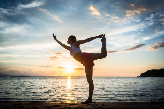 Full length side view of a fit woman practicing on the beach the standing bow pulling pose, for muscular strength and flexibility during summer vacation in Indonesia