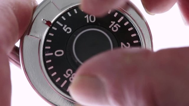 Very close video of unlocking a combination padlock atop a white background.