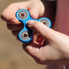 Fototapeta premium girl playing blue metal spinner in hands on the street, female hands holding popular fidget spinner toy on gray background, anxiety relief toy, anti stress and relaxation fidgets.