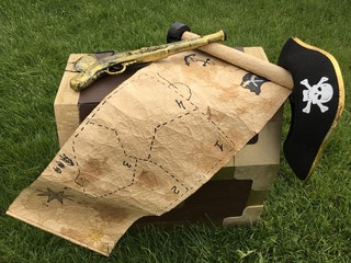 An old treasure map, a pirate hat, a gun and a treasure chest on the lawn