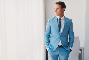 The handsome man in a blue suit. A portrait of the young groom in the interior. Portrait of the successful young businessman