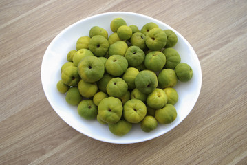 Chaenomeles japonica (known as Maule's quince) green and yellow fruits on the white plate. Wooden background.
