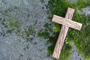 Holzkreuz liegt auf einer Steinplatte mit Moos