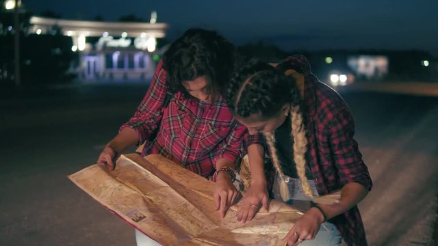 Two young women hitchhiker searching for direction looking at the map, young women hitch-hiking on a road in the city. Slowmotion shot