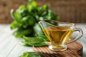 Gravy boat with basil oil and green  leaves on wooden board