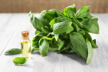 Bottle with basil oil and green leaves on wooden table