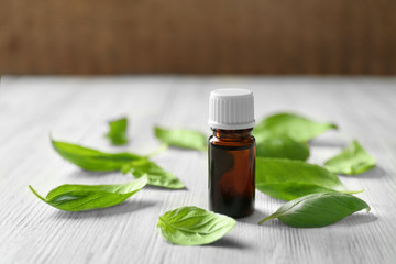 Bottle with basil oil and green leaves on wooden table