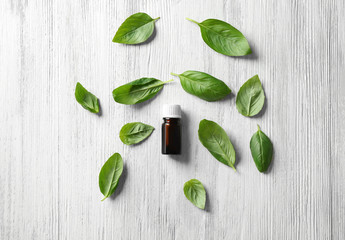 Bottle with basil oil and green leaves on wooden table