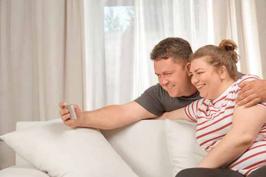 Overweight couple taking selfie on sofa at home