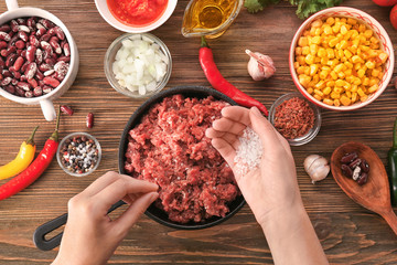 Woman adding salt to raw minced meat in kitchen