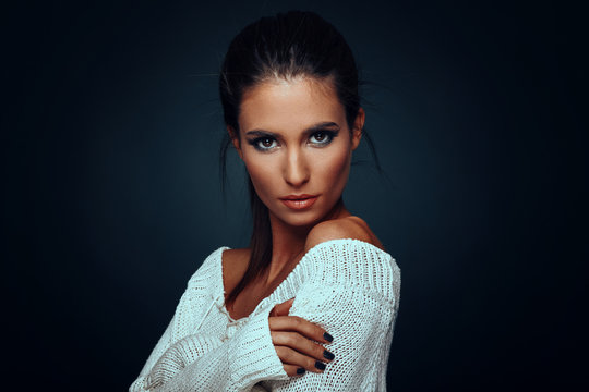 Beautiful woman in white sweater posing in studio on dark background