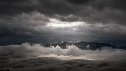 Obraz premium The top of the mountain between two levels of clouds during a storm.