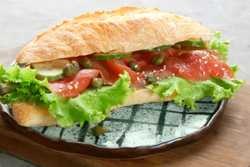 Tasty sandwich with salmon and vegetables on plate