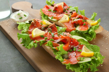 Tasty sandwiches with salmon and lemon on wooden board