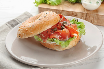 Tasty bagel sandwich with salmon and vegetables on plate