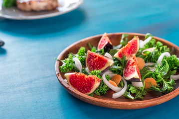 Autumn salad of arugula, figs in a brown earthenware plate on a dark background. top view