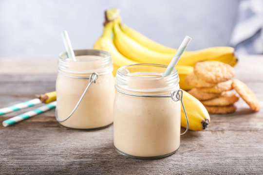 Glass jars with delicious banana smoothie on wooden table