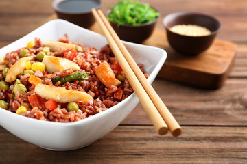 Bowl with brown rice, vegetables and chopsticks on wooden table