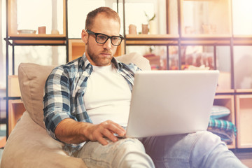 Serious young startupper wearing glasses working on laptop