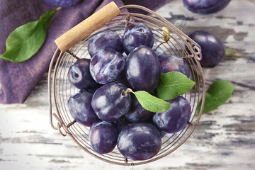 Metal basket with ripe plums on table