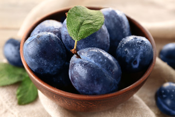 Bowl with ripe plums on table