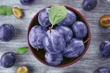 Bowl with ripe plums on wooden background