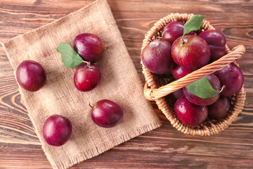 Wicker basket with ripe plums on table