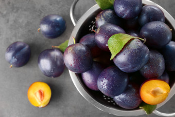 Colander with fresh ripe plums on table