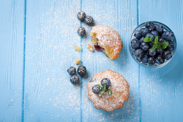 Homemade baked muffin with blueberries, fresh berries, mint, powdered sugar on blue wooden background. Top view.