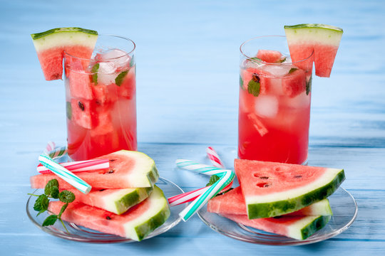 Watermelon lemonade with ice and mint leaves. Homemade lemonade of ripe berry with red and green ripes. Two glasses of watermelon tea. Refreshing summer drink. Cocktail on a wooden background
