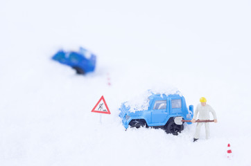 A toy worker with a shovel  removing snow from a toy car.