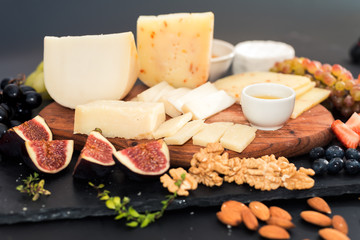 different kinds of cheeses, honey, figs, nuts, grapes, and fruit on a table. Selective focus. Copy space.